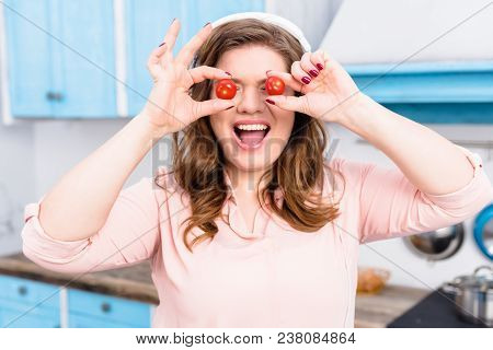 Obscured View Of Overweight Woman In Headphones With Cherry Tomatoes In Hands In Kitchen