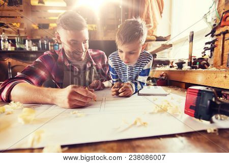 family, carpentry, woodwork and people concept - happy father and little son with blueprint at workshop
