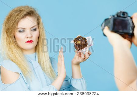 Woman Refuses To Eat Chocolate Cupcake, Man Taking Picture Of Her. Blue Background.