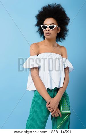 Young African American Woman In Stylish Off-the-shoulder Top And Sunglasses Isolated On Blue