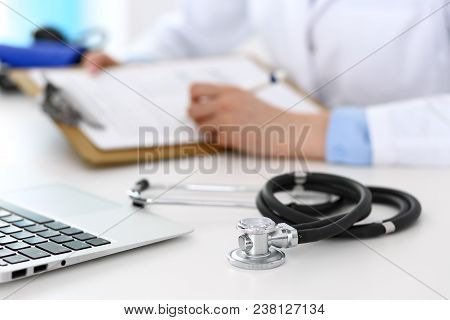 Closeup Of Stethoscope. Female Doctor Fills Up Medical Form While Sitting At The Desk In Hospital. H