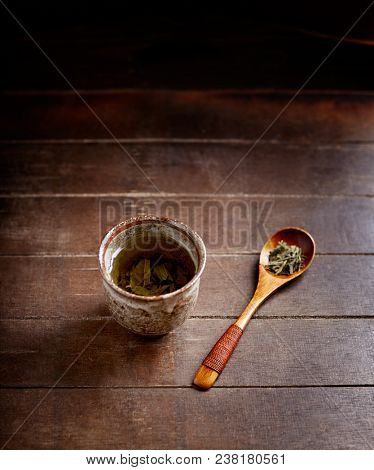 Green tea (sencha) in a traditional, japanese tea cup and sencha leaves on a wooden  tea spoon. Dark wooden background. 