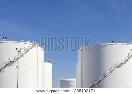 White Tanks In Tank Farm With Iron Staircase Under Blue Sky