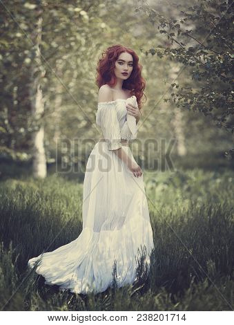 A Sensual Red-haired Girl In A White Dress With Bare Shoulders Holds A White Dove In Her Hand. White