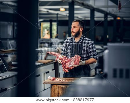 Portrait Of A Bearded Meat Man Dressed In A Fleece Shirt Holds Fresh Cut Meat In A Market.