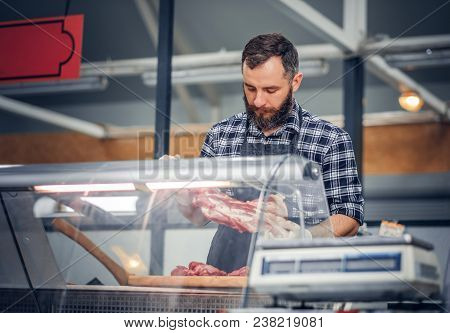 Bearded Meat Seller Dressed In A Fleece Shirt Serving Fresh Cut Meat In A Market.