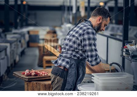 Bearded Butcher Dressed In A Fleece Shirt Serving Fresh Cut Meat In A Market.