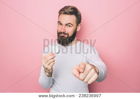 Happy Man Is Holding A Condom And Pointing On Camera. He Is Smiling. Isolated On Pink Background