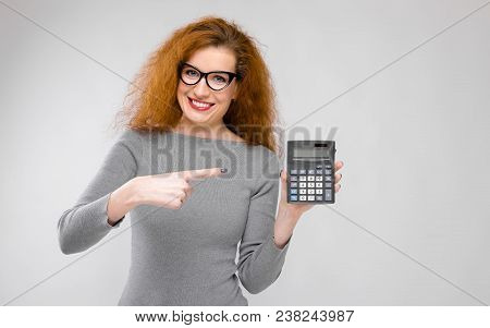 Portrait Of Attractive Serious Businesswoman In Dress And Eyeglasses Pointing At Calculator Isolated