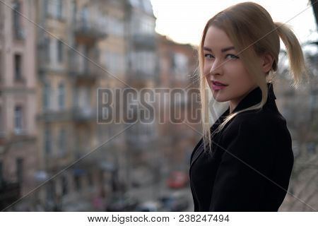 Portrait Of A Young Woman In A Black Suit Close-up Against A Background Of A Blurry City In The Rays