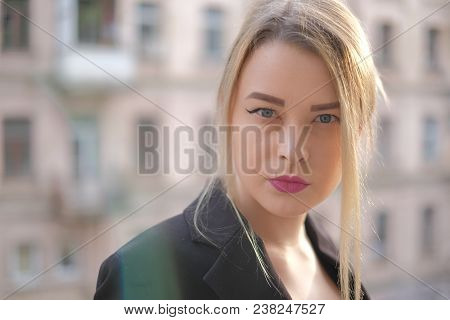 Portrait Of A Young Woman In A Black Suit Close-up Against A Background Of A Blurry City In The Rays