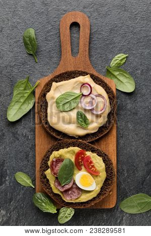 Open faced sausage sandwich canape or crostini on a wooden serving board  on dark stone background closeup. Top view.