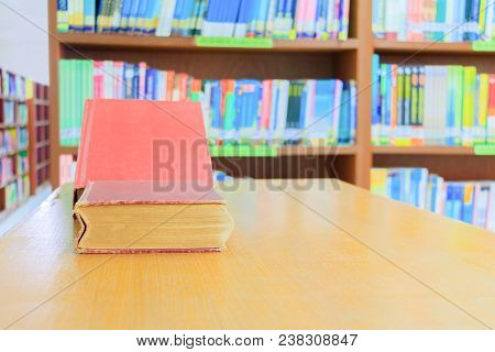 Old Book Red And Heap Treatise In School Library On Wooden Table. Blurry Bookshelves Background. Edu