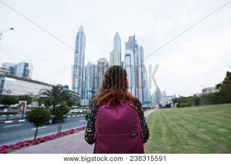 Beautiful Girl With A Backpack Looking At The Tall Beautiful City Buildings Near The Road