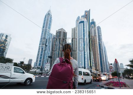 Beautiful Girl With A Backpack Looking At The Tall Beautiful City Buildings Near The Road