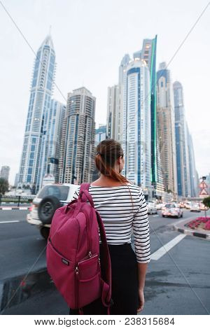 Beautiful Girl With A Backpack Looking At The Tall Beautiful City Buildings Near The Road