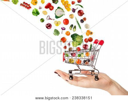 Female Hand Holding Grocery Cart With Vegetables And Fruits Falling In It Isolated On White. Healthy