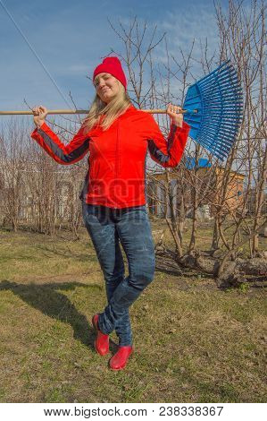 Full Length Portrait Of A Smiling Woman Professional Gardener With A Rake, A Beautiful Blonde Workin