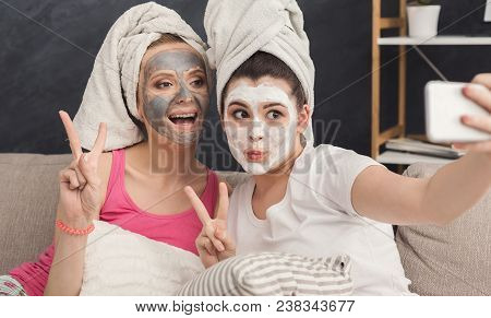 Two Girls With Cosmetic Masks And With Towels On Heads Having Fun And Taking Selfie At Home. Friends