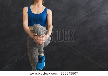 Young Woman Warming Up Before Training At Gym. Unrecognizable Girl Stretching Her Leg At Gray Backgr