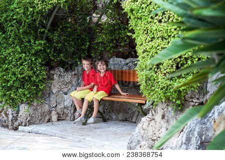Brothers, Sitting On A Bench In Botanical Garden, Having Rest After Long Day Of Walking