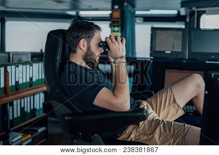 Deck Navigation Officer On The Navigation Bridge. He Looks Through Binoculars. Watchkeeping, Collisi