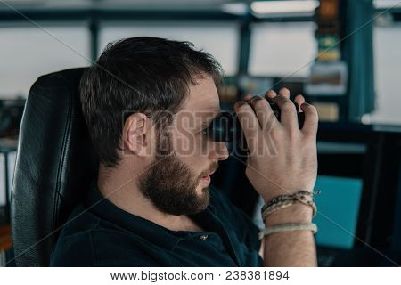Deck Navigation Officer On The Navigation Bridge. He Looks Through Binoculars. Watchkeeping, Collisi