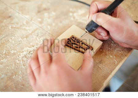 Hands of master of burning ornaments carving wooden board with pyrographic equipment