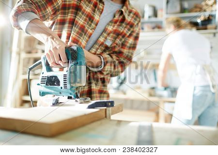 Hands of female worker with electric fretsaw working with wooden boards