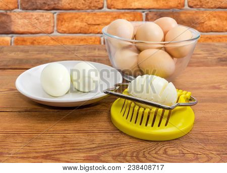 Egg Slicer With Partly Sliced Egg In It, Boiled Peeled And Not Cleaned Eggs In Different Dishes On A