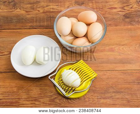 Egg Slicer With Partly Sliced Egg In It, Two Boiled Peeled Eggs On A Saucer And Not Cleaned Eggs In 