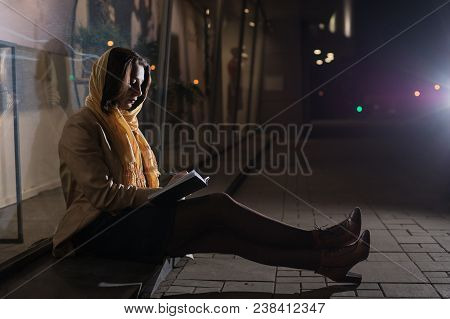 Girl Brunette Sitting Near In The Shopwindow On The Night City Street In A Cold Time