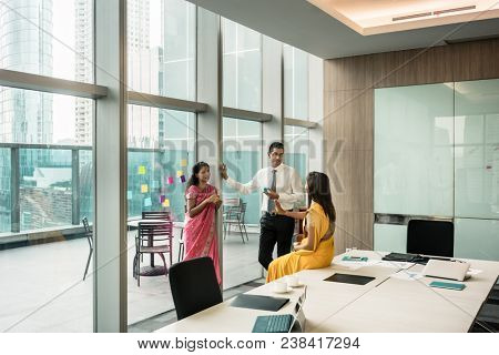 Three Indian employees talking during break in the meeting room of a modern business building