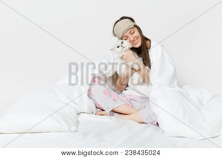 Calm Young Woman Sitting In Bed With Sleep Mask On Eyes Isolated On White Background. Beauty Female