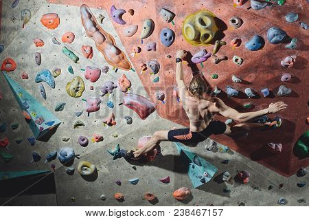 Workout Exercise. Back View Of A Man Climber Climbs Indoors In Bouldering Gym. Athletic Man Climbing