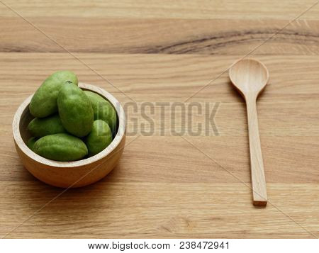 A Group Of Green Hog Plums Fruit In Wooden Bowl With Wooden Spoon Over Bright Wooden Background With