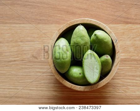 A Group Of Green Hog Plums Fruit, Which Look Like Small Mango, In Wooden Bowl Over Bright Wooden Bac