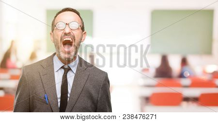 Teacher man using glasses stressful, terrified in panic, shouting exasperated and frustrated. Unpleasant gesture. Annoying work drives me crazy at classroom