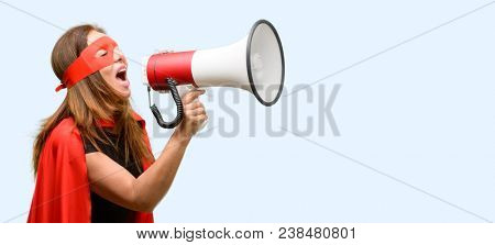 Middle age super hero woman wearing red mask and cape communicates shouting loud holding a megaphone, expressing success and positive concept, idea for marketing or sales isolated blue background