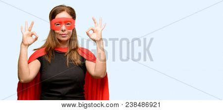 Middle age super hero woman wearing red mask and cape doing ok sign gesture with both hands expressing meditation and relaxation isolated blue background