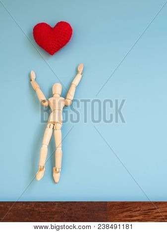 Wooden Puppet Jumping From The Wooden Floor In The Air To Catch The Red Heart Floating In The Sky. W