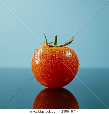 Tomato with drops and a green tail isolated on glossy blue background