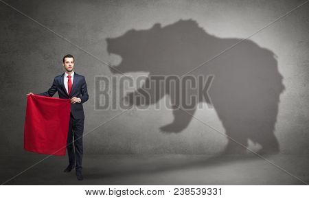 Businessman standing with red cloth in his hand and big bear shadow on his background