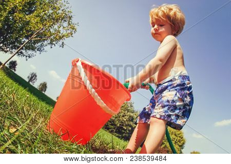 Toddler boy playing with a hose in the backyard filling a bucket