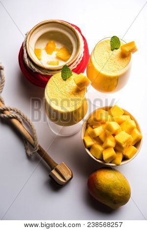 Mango Lassi Or Smoothie In Big Glass Or Small Bottles With Curd, Cut Fruit Pieces And Blender. Moody