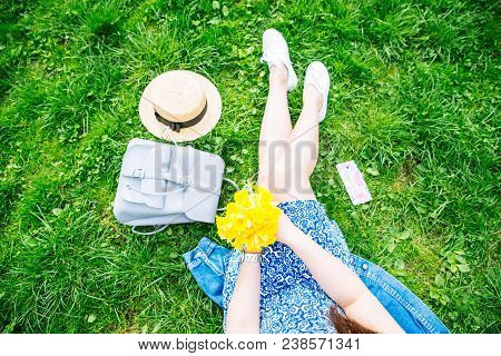 Woman Sitting On Grass In City Park With Yellow Flowers