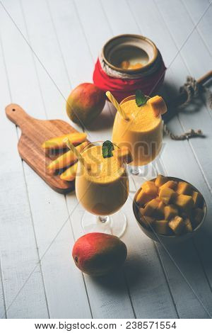 Mango Lassi Or Smoothie In Big Glass Or Small Bottles With Curd, Cut Fruit Pieces And Blender. Moody