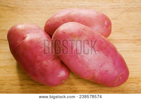 Three Red Desiree Potatoes On A Wooden Board