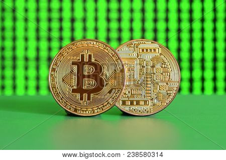 Two Gold Bitcoins Lie On The Green Surface On The Background Of The Display, Which Shows The Process