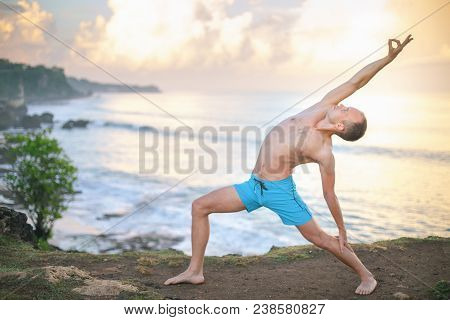 Handsome Man Doing Yoga Near The Beach With Blue Sky And Sea Background. Relaxing And Healthy Lifest